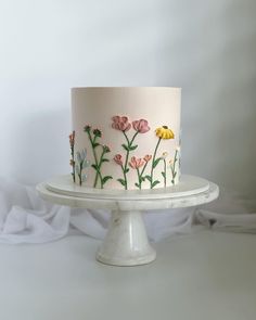 a white cake with pink and yellow flowers painted on the top is sitting on a pedestal