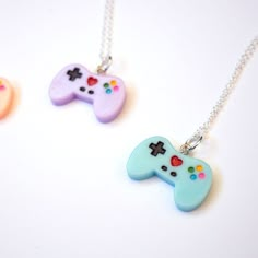 three necklaces that have different colored video game controllers on them, one is blue and the other is pink