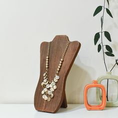 a wooden stand with a necklace on it next to two vases and a plant