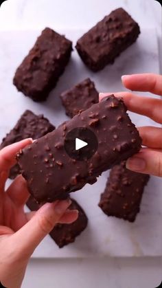 someone is holding a chocolate bar in front of some pieces of chocolate on a white surface