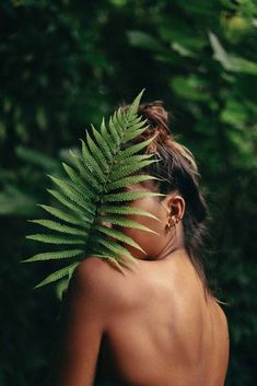 a woman with her back turned to the camera, holding a fern leaf in front of her face