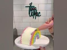 a person cutting a rainbow cake with a knife on a white plate in front of a sign that says tea cupcake