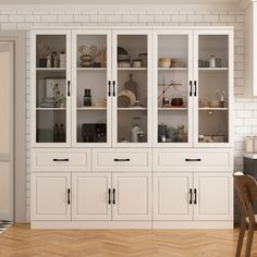 a kitchen with white cabinets and wood flooring next to a dining room table in front of a brick wall