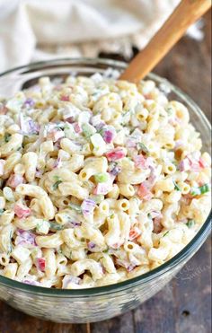 a glass bowl filled with macaroni salad on top of a wooden table next to a white towel