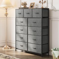 a large gray dresser with drawers in a white room next to a lamp and pictures on the wall