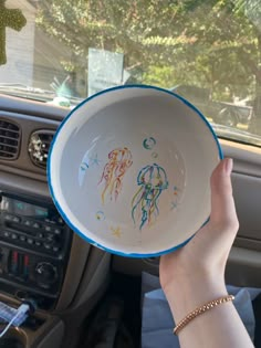 a person is holding up a bowl with drawings on it in the backseat of a car