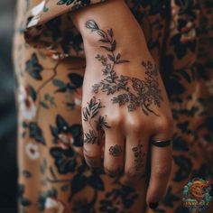 a woman's hand with tattoos and flowers on her left wrist, in front of a floral print dress