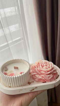 a person holding a white tray with a pink flower on it and a candle in the middle