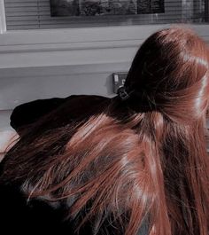 a woman with long red hair sitting in front of a window looking out the window