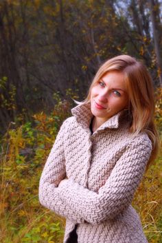 a woman standing in the grass with her arms crossed and wearing a sweater over her shoulders