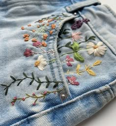 a pair of jeans with embroidered flowers on them sitting on top of a white surface