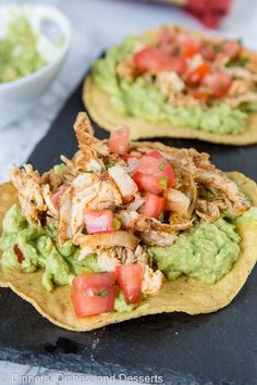 two tortilla shells topped with chicken, tomatoes and avocado on a black tray