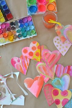 some paper hearts are sitting on a table with paint and watercolors in the background