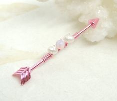 a pink and white arrow shaped pin with pearl beads on it's end, sitting next to some crystals