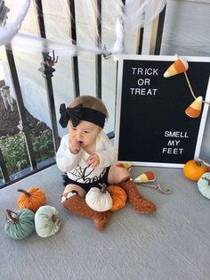 a baby sitting on the ground next to some fake pumpkins and other halloween decorations