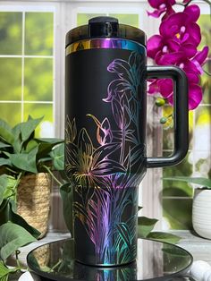 a black coffee mug sitting on top of a glass table next to flowers and potted plants