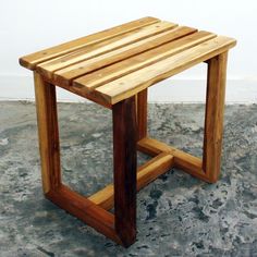 a small wooden table sitting on top of a cement floor next to a white wall