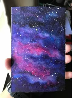 a hand holding up a piece of paper with watercolor paint on it and stars in the sky