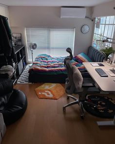 a room with a bed, desk and computer on the floor in front of a window