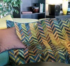 a couch covered with colorful pillows and blankets in a living room next to a book shelf