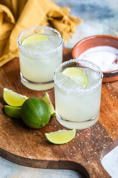 two margaritas on a wooden cutting board with limes and salt in the background