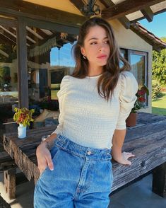 a woman standing in front of a wooden bench wearing high waisted jeans and a white top