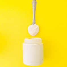 a spoon full of cream sitting on top of a yellow table next to a jar