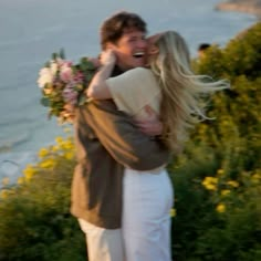 a man and woman hugging each other in front of the ocean with wildflowers