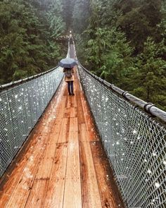 a person walking across a bridge with an umbrella over their head and trees in the background