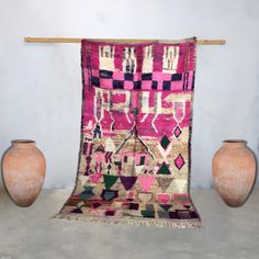 two vases and a rug on display in a room with a wall hanging from the ceiling