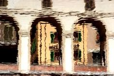 the reflection of an old building and its columns in water with reflections on it's surface