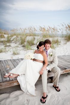 a bride and groom sitting on a bench at the beach