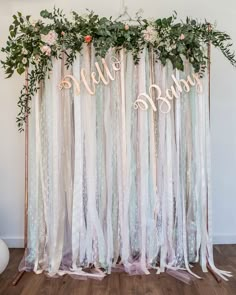 the backdrop is decorated with white and pink ribbons, greenery, and hello baby letters