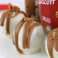 three chocolate covered desserts on a white plate with a red cup in the background