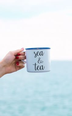 a woman holding a white and blue cup with the words sea & tea on it