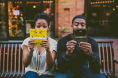 a man and woman sitting on a bench looking at their cell phones while they both look at the screen