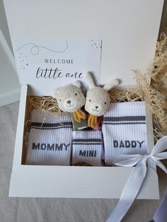 two stuffed animals are in a box with baby socks and a welcome little one sign