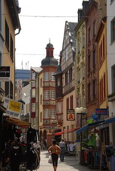 a woman is walking down the street in an old european town with shops and buildings