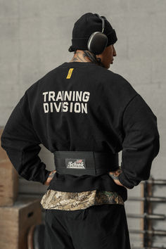 a man with headphones standing in front of a wall wearing a training division jacket