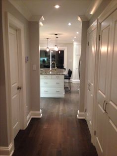 an empty hallway leading to a kitchen with white cabinets and dark wood flooring on both sides