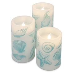 three white candles with blue sea shells and seashells painted on them, sitting next to each other