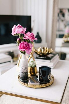 pink flowers are in a vase on a coffee table next to two black mugs