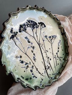 a white and green plate with black flowers on it sitting on top of a pink napkin