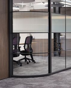 an office with glass walls and chairs in the middle, looking out into the open space