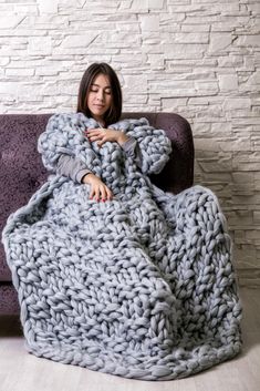 a woman laying on a couch wrapped in a chunky gray blanket with her hands under her chest