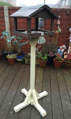 a bird house sitting on top of a wooden deck next to potted plants and trees