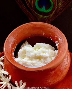 a bowl filled with whipped cream sitting on top of a wooden table next to a peacock's tail