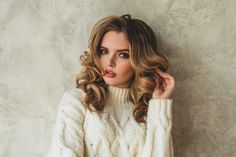 a woman with long hair wearing a white sweater and holding her hand to her ear