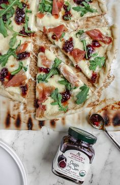 a pizza sitting on top of a pan covered in cheese and veggies next to a jar of jam