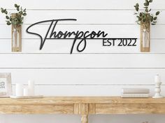 a wooden table topped with vases filled with flowers and greenery next to a white wall